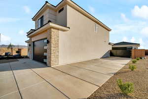 View of home's exterior featuring stone siding, an attached garage, concrete driveway, and stucco siding