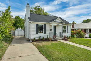 Bungalow-style home with an outdoor structure, a front yard, a chimney, a garage, and roof with shingles