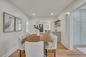 Dining space featuring arched walkways, light wood-style floors, recessed lighting, and baseboards