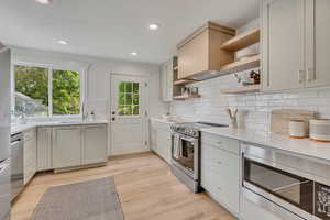 Kitchen featuring stainless steel appliances, open shelves, a sink, light countertops, and light wood finished floors