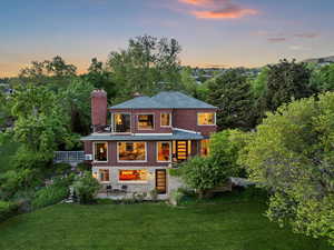 Back of house at dusk with a chimney, a yard, brick siding, and a balcony