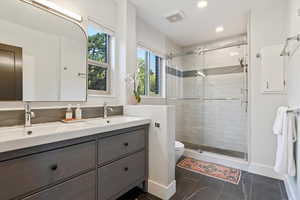Full bath featuring double vanity, a stall shower, toilet, recessed lighting, and baseboards