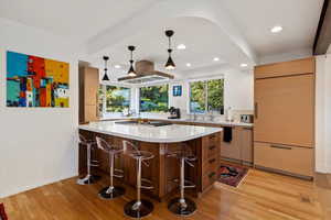 Kitchen featuring paneled refrigerator, stainless steel gas stovetop, a kitchen bar, light countertops, and recessed lighting