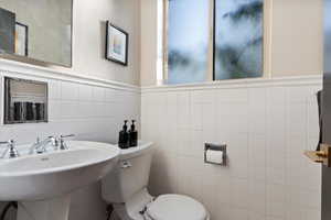 Half bathroom featuring tile walls, toilet, and a sink