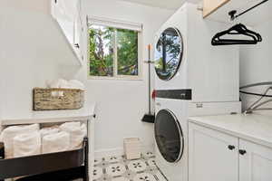 Laundry area with cabinet space, stacked washer / drying machine, baseboards, and light tile patterned flooring