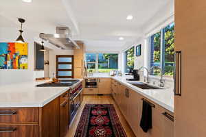 Kitchen featuring a sink, range hood, light wood-style flooring, light countertops, and stovetop