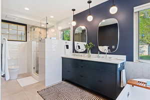 Bathroom featuring tile walls, a stall shower, double vanity, a bathtub, and toilet