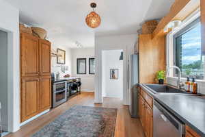Kitchen with stainless steel appliances, a sink, wall chimney range hood, brown cabinetry, and light wood finished floors