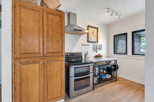 Kitchen featuring range with two ovens, wall chimney range hood, light wood-style floors, brown cabinetry, and a textured ceiling
