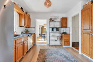 Kitchen with appliances with stainless steel finishes, light wood-style floors, backsplash, and brown cabinetry