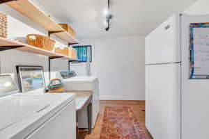 Washroom with washer and clothes dryer, light wood finished floors, baseboards, and track lighting