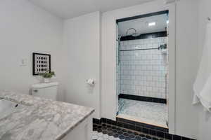 Full bath with vanity, a tile shower, tile patterned flooring, and toilet