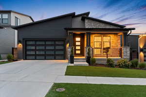 Modern home with stone siding, driveway, an attached garage, covered porch, and a front lawn