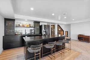Indoor wet bar with stainless steel refrigerator with ice dispenser, baseboards, recessed lighting, and a tray ceiling