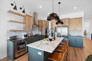 Kitchen with wall chimney range hood, appliances with stainless steel finishes, beverage cooler, tasteful backsplash, and open shelves