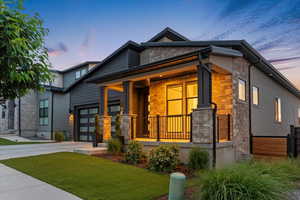 Modern home featuring stone siding, a porch, concrete driveway, an attached garage, and a front lawn