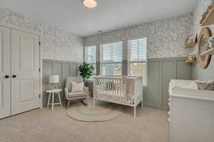 Secondary Bedroom with wallpapered walls, a crib, light colored carpet, a wainscoted wall, and a decorative wall