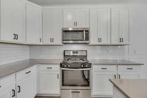 Kitchen with stainless steel appliances, white cabinetry, and tasteful backsplash