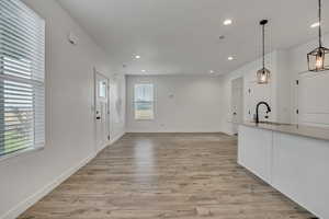 Kitchen featuring a sink, recessed lighting, hanging light fixtures, light wood-style floors, and baseboards