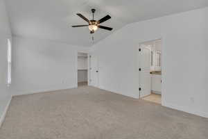 Primary suite with lofted ceiling, light carpet, baseboards, a spacious closet, and connected bathroom shown vacant