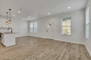 Kitchen with a sink, light wood-type flooring, white cabinets, pendant lighting, and light countertops