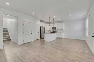 Unfurnished living room with stairway, light wood-style floors, recessed lighting, a sink, and baseboards