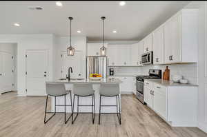 Kitchen featuring stainless steel appliances, pendant lighting, white cabinetry, a kitchen bar, and light wood-style flooring