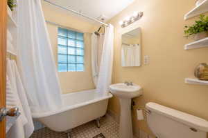 Bathroom featuring toilet, a sink, baseboards, and shower / bathtub combination with curtain