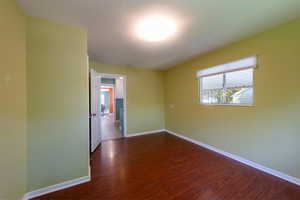 Spare room featuring dark wood-style flooring and baseboards