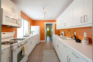 Kitchen featuring white appliances, a sink, light countertops, white cabinetry, and tile patterned flooring
