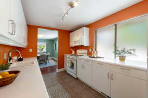 Kitchen featuring white appliances, a sink, light countertops, white cabinetry, and dark tile patterned flooring
