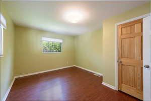 Spare room featuring dark wood-style floors and baseboards