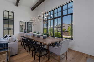 Dining space with a chandelier, beamed ceiling, a towering ceiling, wood finished floors, and baseboards