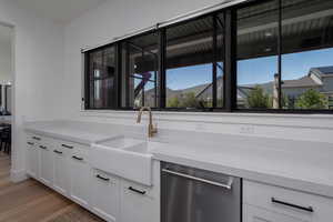 Kitchen featuring stainless steel dishwasher, a sink, light wood finished floors, and white cabinets