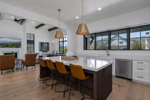 Kitchen with stainless steel dishwasher, a sink, white cabinetry, beamed ceiling, and a center island