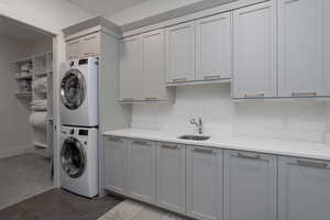 Laundry room with stacked washer / dryer, cabinet space, dark tile patterned flooring, and dark colored carpet