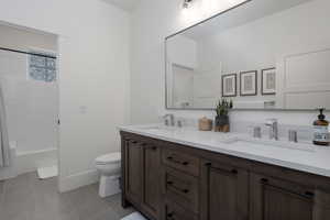 Bathroom with toilet, double vanity, bathtub / shower combination, and tile patterned floors