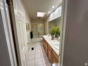 Main Bathroom with a skylight, double vanity, bath / shower combo with glass door, toilet, and tile patterned flooring