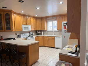 Kitchen featuring white appliances,  a sink, a breakfast bar area.and glass insert cabinets