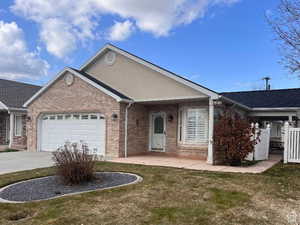 Single story home with an attached garage, brick siding, driveway, a front yard, and roof with shingles