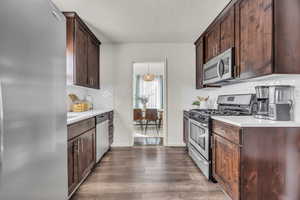 Kitchen featuring appliances with stainless steel finishes, light countertops, dark wood-type flooring, dark brown cabinets, and a textured ceiling