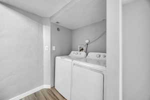Laundry area featuring washer and dryer, light wood-type flooring, a textured ceiling, baseboards, and a textured wall