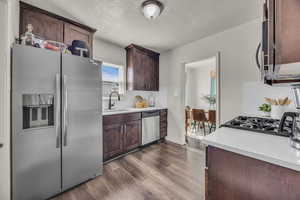 Kitchen with stainless steel appliances, a sink, dark wood-type flooring, a textured ceiling, and light countertops