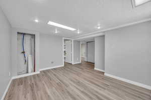 Below grade area with a textured ceiling, baseboards, and light wood-type flooring