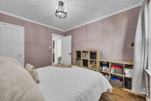 Bedroom with wood finished floors, crown molding, a textured ceiling, and a chandelier