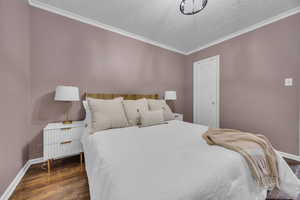 Bedroom with wood finished floors, ornamental molding, baseboards, and a textured ceiling