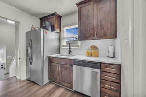 Kitchen with appliances with stainless steel finishes, a sink, wood finished floors, backsplash, and light countertops