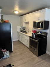 Kitchen featuring appliances with stainless steel finishes, a sink, backsplash, baseboards, and white cabinetry