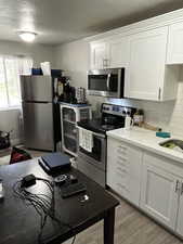Kitchen featuring appliances with stainless steel finishes, white cabinetry, backsplash, light countertops, and light wood-style floors