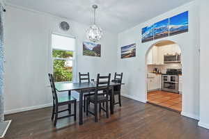 Dining room featuring arched walkways, ornamental molding, dark wood-style floors, a chandelier, and baseboards
